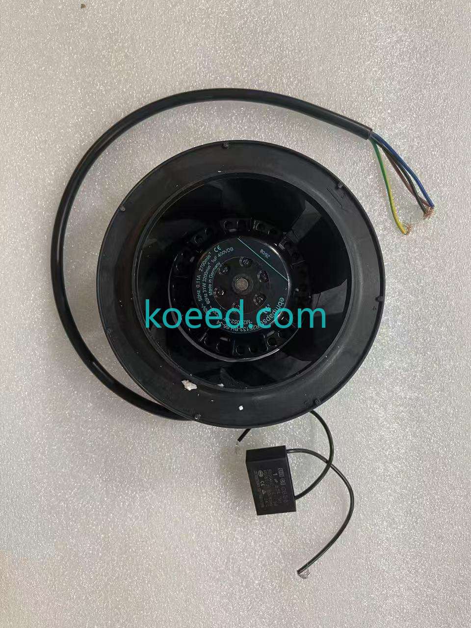 Black fan face on white foam with an ebmpapst R2E133-BH66-34 label, loose coloured cable ends and a separate rectangular electrical component.